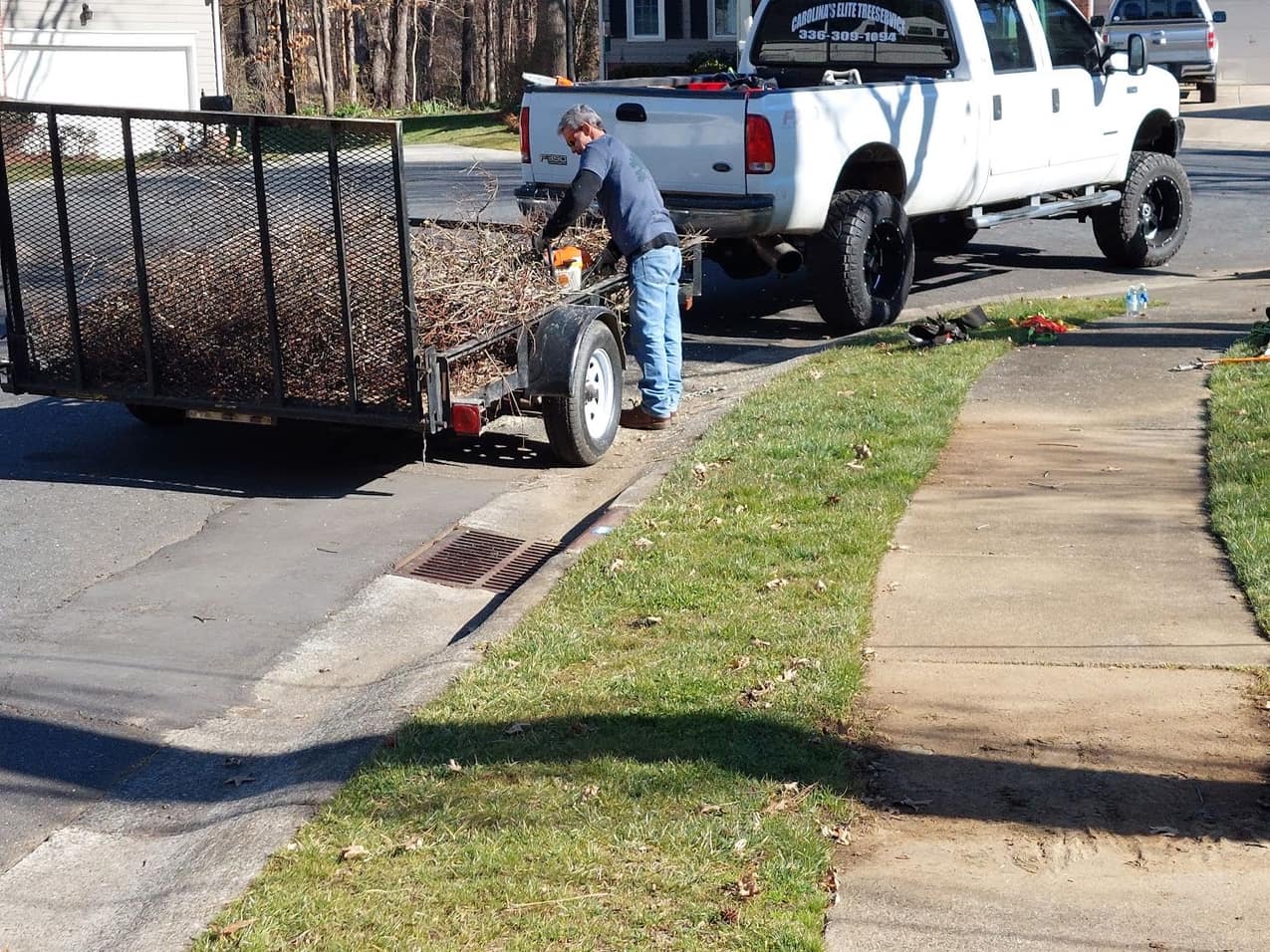 Carolina's Elite pickup truck and dump trailer parked at a job on a neighborhood street